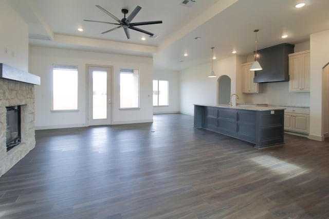 kitchen with a stone fireplace, open floor plan, wall chimney exhaust hood, a center island with sink, and pendant lighting