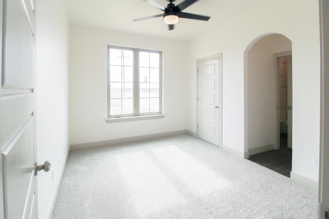 spare room featuring ceiling fan, arched walkways, dark carpet, and baseboards