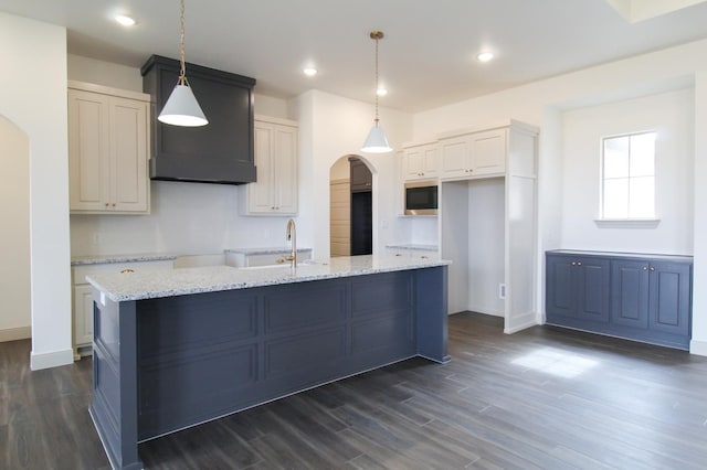 kitchen featuring arched walkways, white cabinets, decorative light fixtures, a kitchen island with sink, and built in microwave