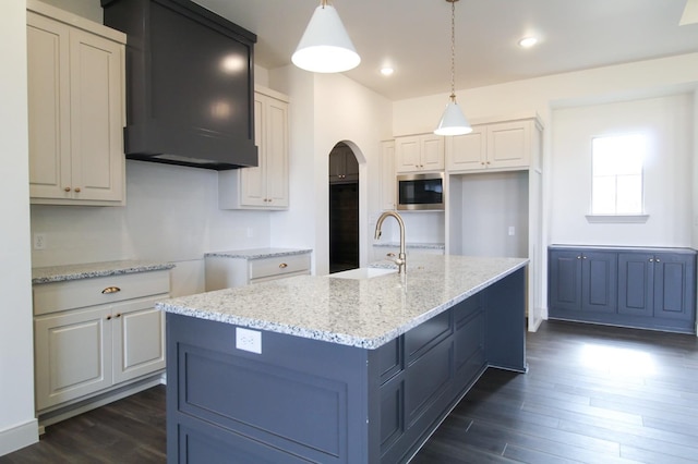 kitchen with a center island with sink, white cabinets, stainless steel microwave, pendant lighting, and a sink