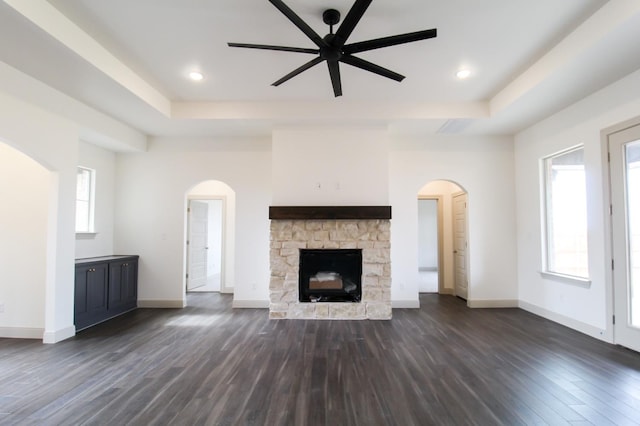 unfurnished living room with a tray ceiling, dark wood finished floors, and arched walkways