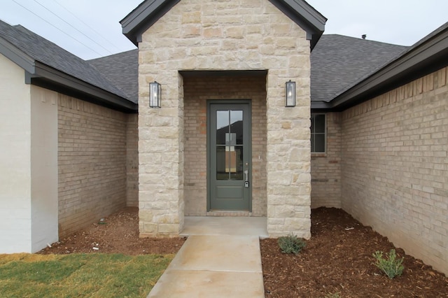 view of exterior entry featuring stone siding, brick siding, and roof with shingles