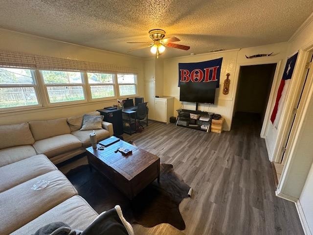 living room with dark wood-type flooring, ceiling fan, ornamental molding, and a textured ceiling