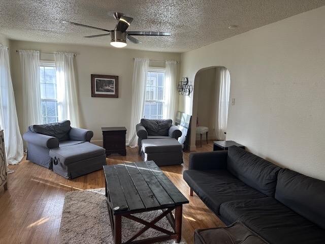 living room featuring wood-type flooring, ceiling fan, and a textured ceiling