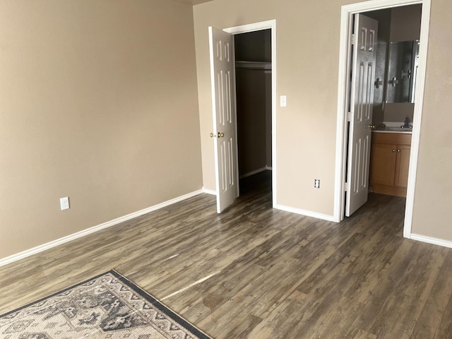 unfurnished bedroom featuring a walk in closet, sink, dark hardwood / wood-style flooring, and a closet