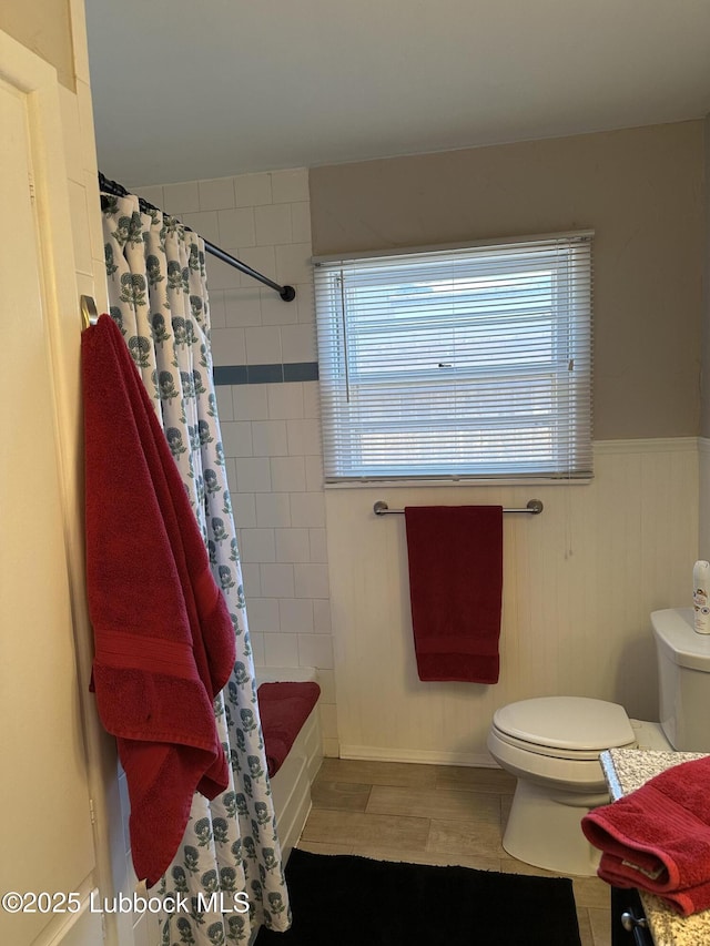 2326 58th St, Lubbock, TX 79412 - full bathroom with wood finished floors, shower / bath combo with shower curtain, and a wainscoted wall