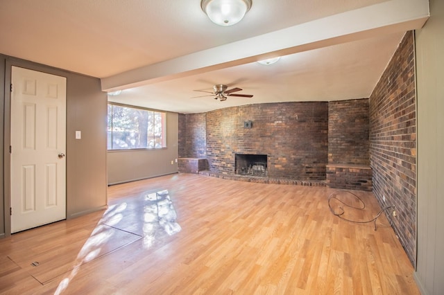 unfurnished living room featuring ceiling fan, brick wall, a brick fireplace, and light hardwood / wood-style flooring