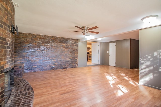 empty room featuring ceiling fan, brick wall, a brick fireplace, and light wood-type flooring