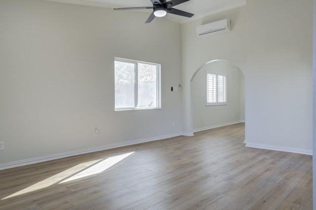 spare room with ceiling fan, light wood-type flooring, a wall unit AC, and a towering ceiling