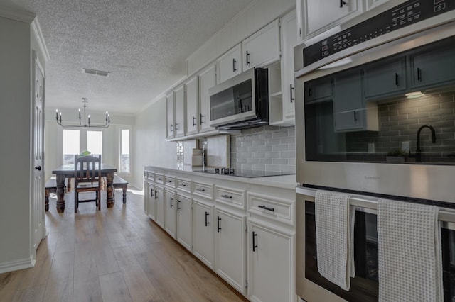 kitchen with white cabinetry, a chandelier, light wood-type flooring, appliances with stainless steel finishes, and backsplash