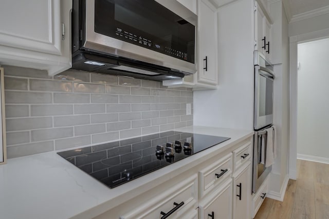 kitchen featuring white cabinetry, ornamental molding, appliances with stainless steel finishes, light hardwood / wood-style floors, and decorative backsplash