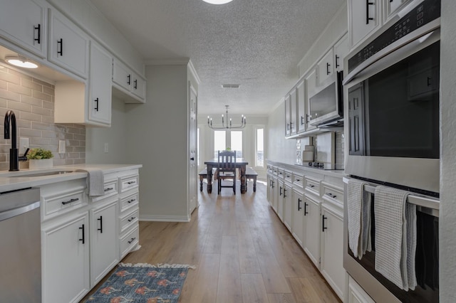 kitchen featuring appliances with stainless steel finishes, white cabinets, light hardwood / wood-style floors, and decorative backsplash