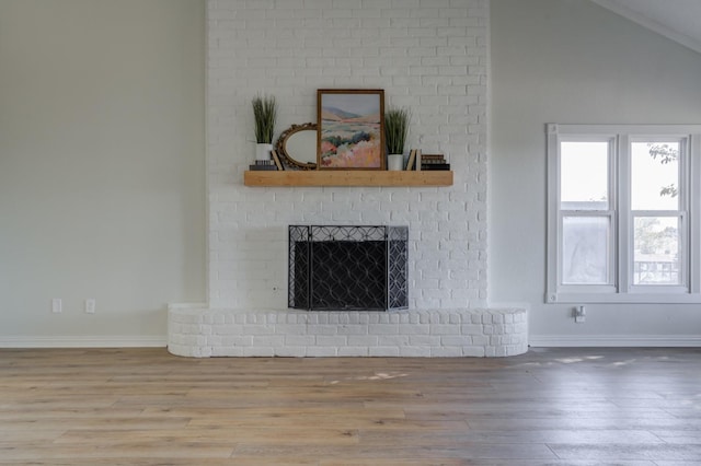 unfurnished living room with hardwood / wood-style flooring, a brick fireplace, and lofted ceiling