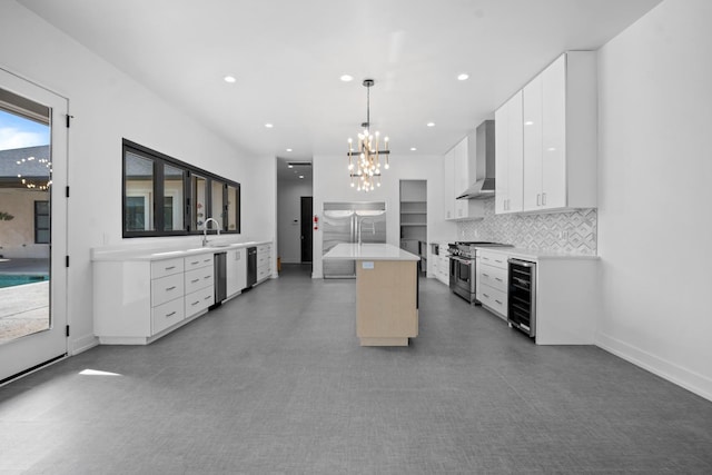 kitchen with decorative light fixtures, high quality appliances, white cabinets, a kitchen island with sink, and wall chimney range hood