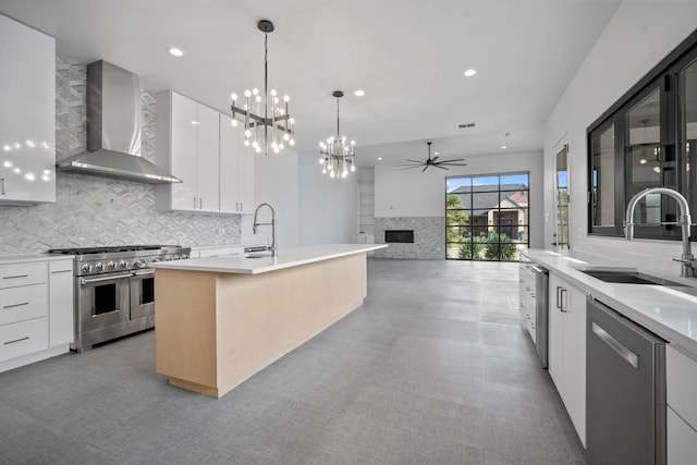 kitchen with a center island with sink, white cabinetry, appliances with stainless steel finishes, and wall chimney range hood