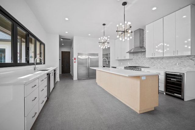 kitchen with white cabinetry, beverage cooler, wall chimney range hood, stainless steel appliances, and a center island with sink