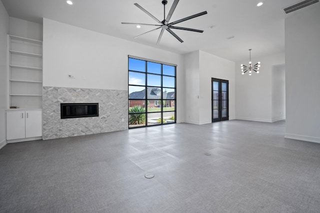 unfurnished living room with a high ceiling, a tile fireplace, ceiling fan with notable chandelier, and french doors