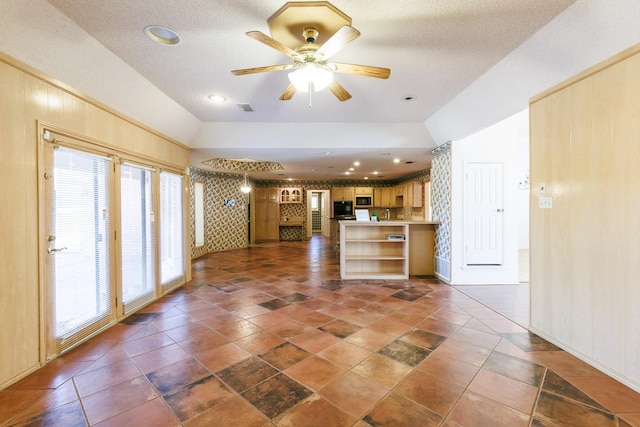 kitchen featuring lofted ceiling, wooden walls, light brown cabinetry, and ceiling fan