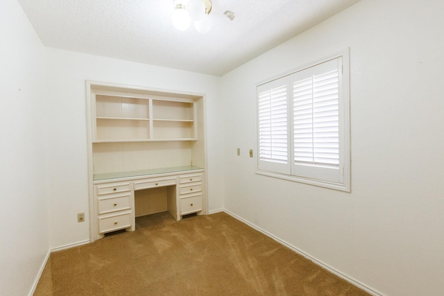 unfurnished office with built in desk, light colored carpet, and a textured ceiling