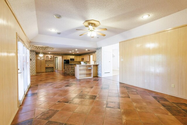 unfurnished living room featuring ceiling fan, wooden walls, vaulted ceiling, and a textured ceiling