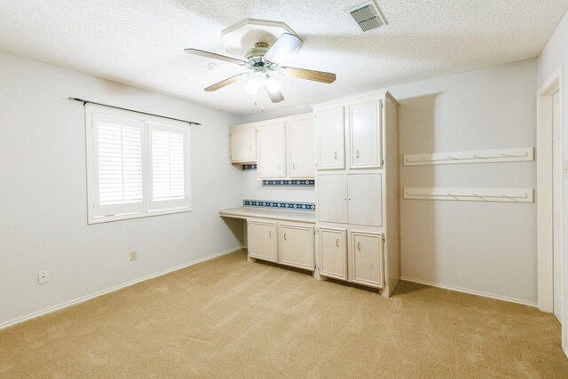 unfurnished office featuring light carpet, built in desk, and a textured ceiling