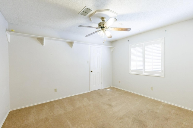 spare room featuring ceiling fan, light colored carpet, and a textured ceiling