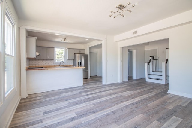 kitchen featuring hardwood / wood-style flooring, stainless steel fridge, gray cabinetry, decorative backsplash, and kitchen peninsula