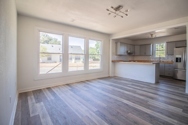 kitchen featuring gray cabinets, dark hardwood / wood-style floors, stainless steel refrigerator with ice dispenser, tasteful backsplash, and kitchen peninsula