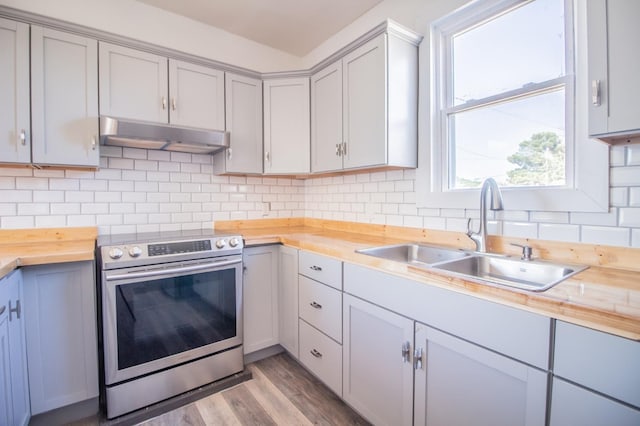 kitchen featuring butcher block countertops, tasteful backsplash, sink, stainless steel range with electric cooktop, and light hardwood / wood-style flooring