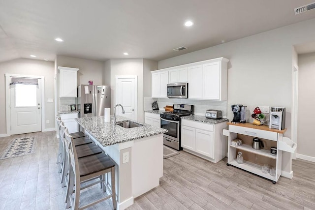 kitchen featuring white cabinetry, sink, a kitchen island with sink, stainless steel appliances, and light stone countertops