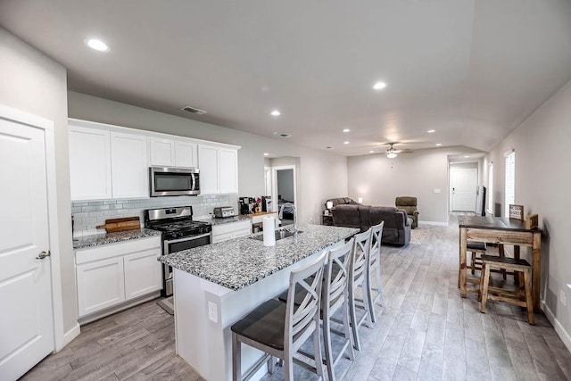 kitchen with sink, white cabinetry, light stone counters, appliances with stainless steel finishes, and an island with sink