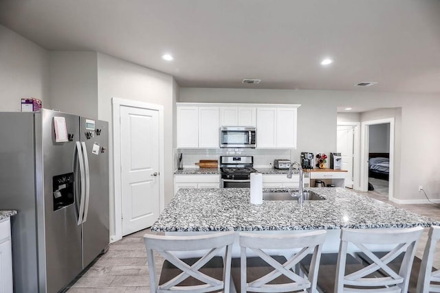 kitchen with appliances with stainless steel finishes, sink, white cabinets, and light stone counters