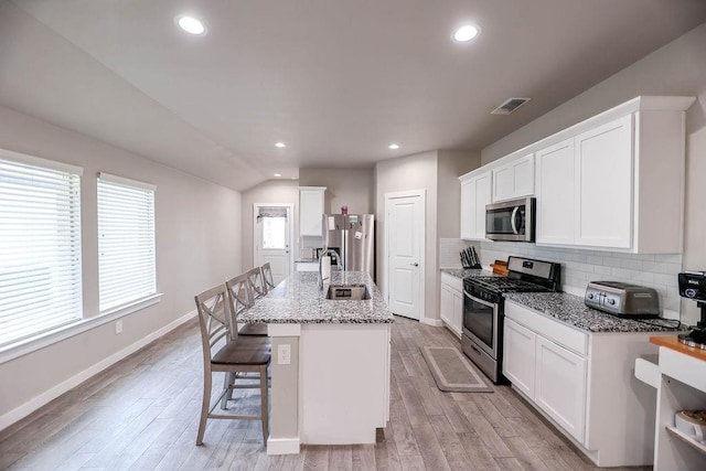 kitchen featuring a kitchen island with sink, light stone countertops, white cabinetry, and stainless steel appliances