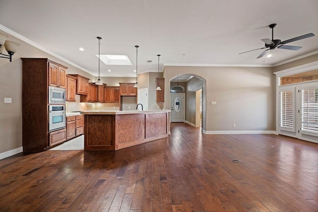 kitchen featuring appliances with stainless steel finishes, decorative light fixtures, a large island with sink, crown molding, and dark wood-type flooring