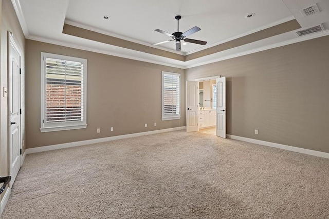 unfurnished bedroom with connected bathroom, light carpet, ornamental molding, a raised ceiling, and ceiling fan