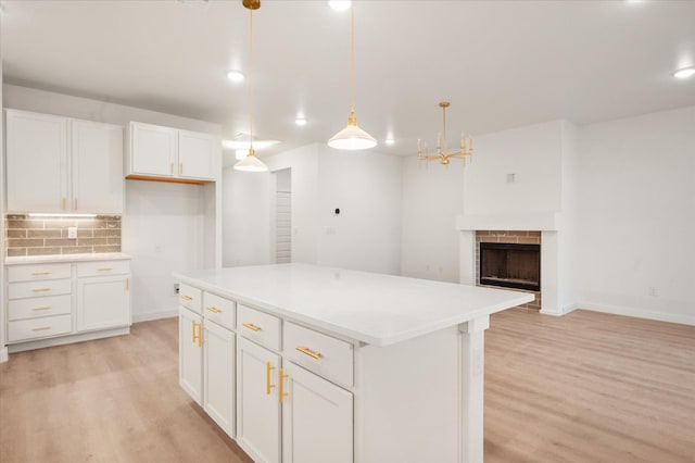 kitchen with white cabinetry, hanging light fixtures, backsplash, light hardwood / wood-style floors, and a kitchen island