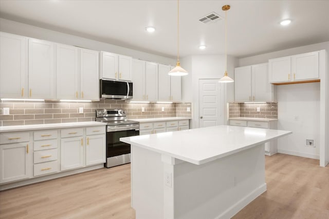 kitchen with a kitchen island, appliances with stainless steel finishes, white cabinets, hanging light fixtures, and light hardwood / wood-style flooring