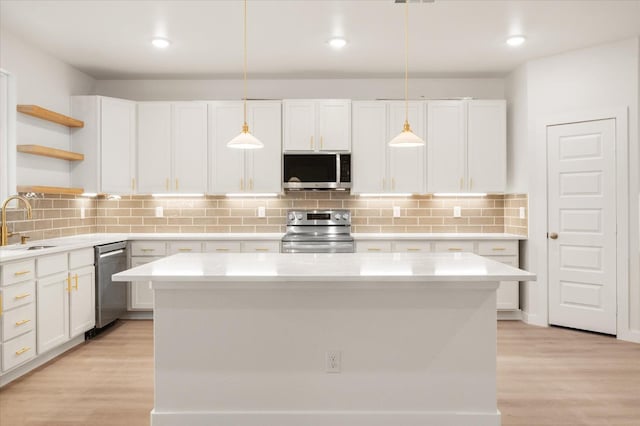 kitchen with stainless steel appliances, a kitchen island, pendant lighting, and white cabinets