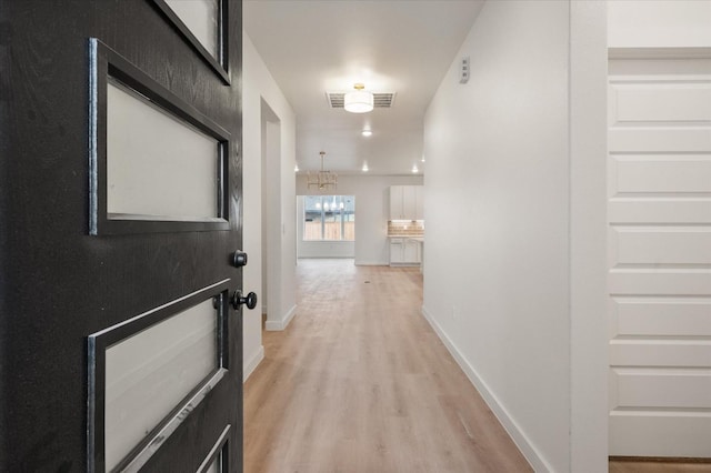 corridor with an inviting chandelier and light hardwood / wood-style floors