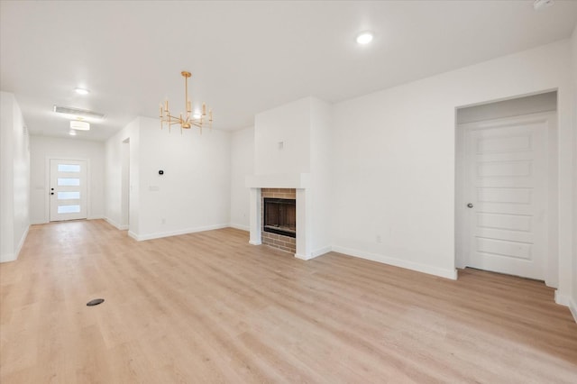 unfurnished living room with a brick fireplace, light hardwood / wood-style floors, and a chandelier