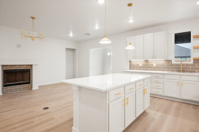 kitchen with sink, light hardwood / wood-style flooring, a kitchen island, pendant lighting, and white cabinets