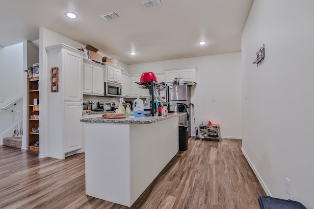 kitchen with light stone counters, a center island with sink, stainless steel appliances, light hardwood / wood-style floors, and white cabinets