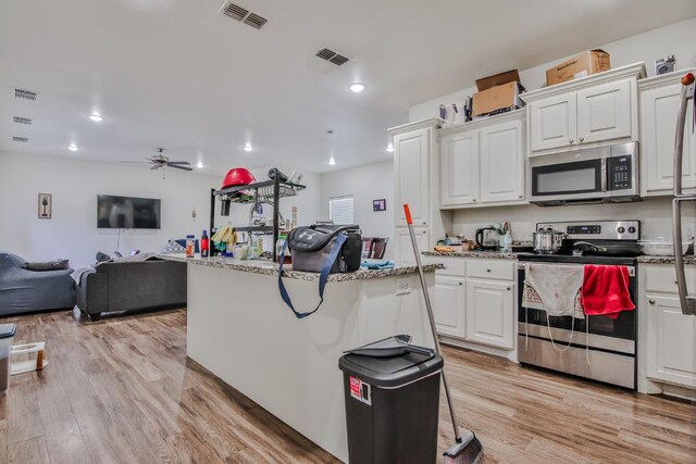 kitchen with light hardwood / wood-style flooring, appliances with stainless steel finishes, white cabinetry, a kitchen island with sink, and light stone counters