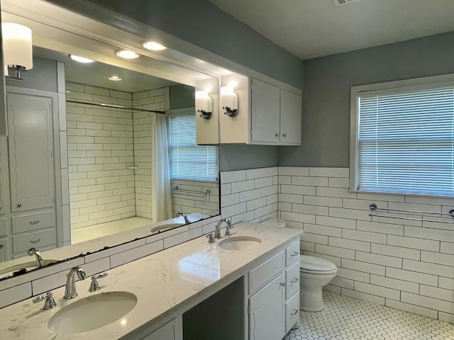 bathroom featuring tile walls, tile patterned flooring, tiled shower, vanity, and toilet