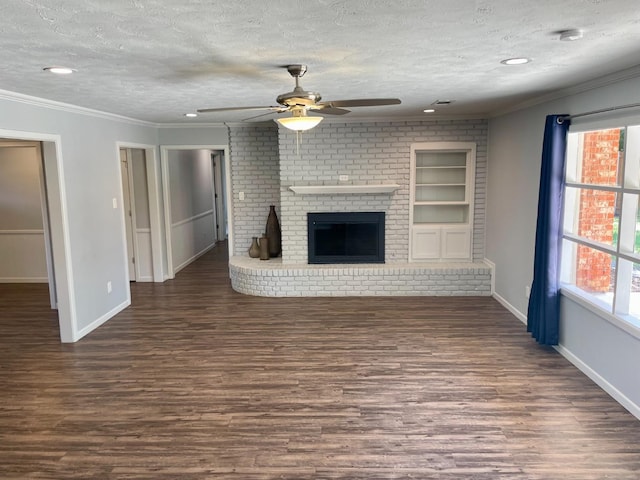 unfurnished living room featuring a brick fireplace, crown molding, dark wood-type flooring, and a textured ceiling