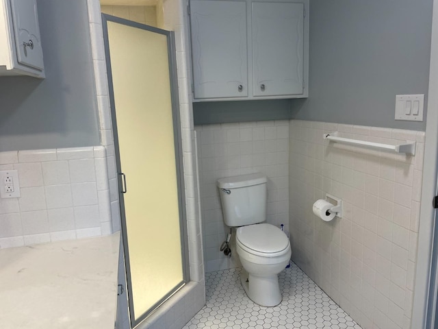 bathroom featuring tile patterned floors, toilet, a shower with shower door, and tile walls