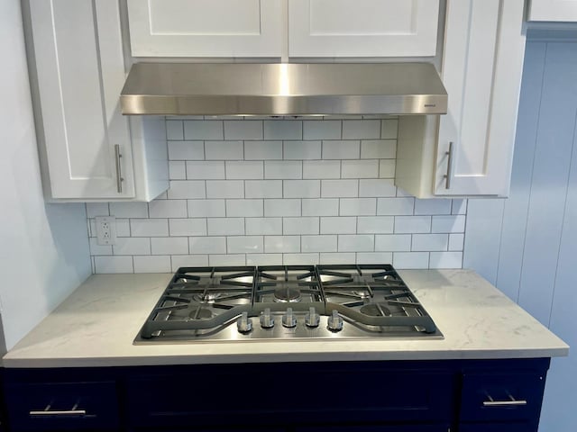 kitchen with light stone counters, tasteful backsplash, white cabinets, exhaust hood, and stainless steel gas stovetop