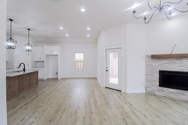 unfurnished living room with a stone fireplace, sink, and light hardwood / wood-style flooring