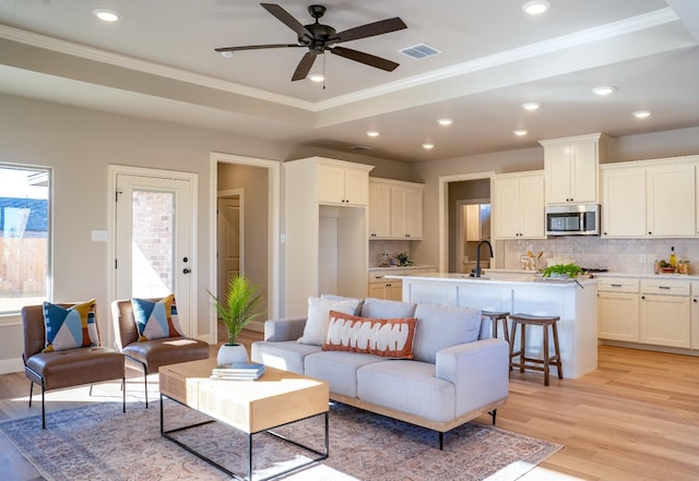 living room with crown molding, a tray ceiling, ceiling fan, and light hardwood / wood-style flooring