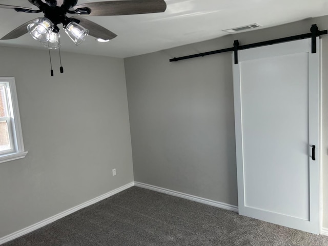 unfurnished room with ceiling fan, a barn door, and dark carpet